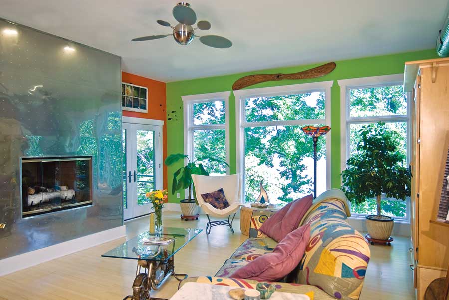 A wall of windows and adjoining porch tie the living room to the wooded backyard. A sleek metal fireplace surround and mellow bamboo floors balance the couple’s bold paint and décor choices.
